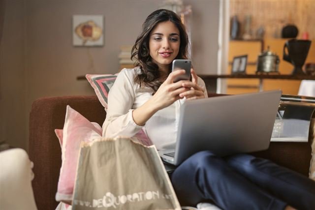 Mujer sonriente revisando mensajes y redes sociales en su celular desde el sillón